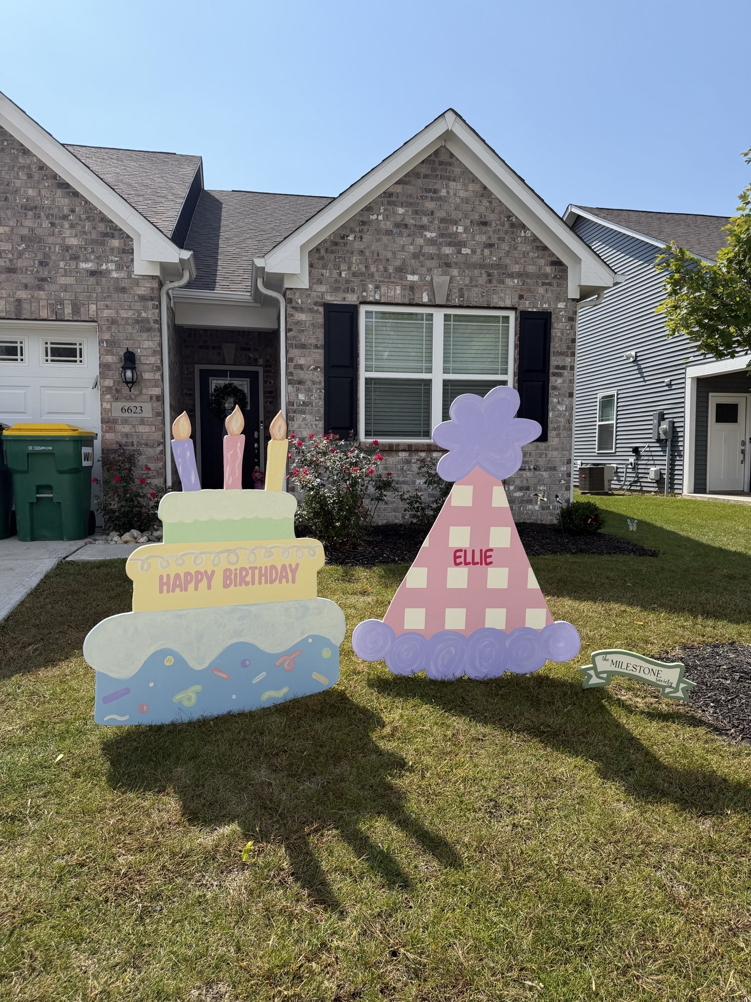 Pastel birthday cake and personalized pink party hat signs installed in a front yard