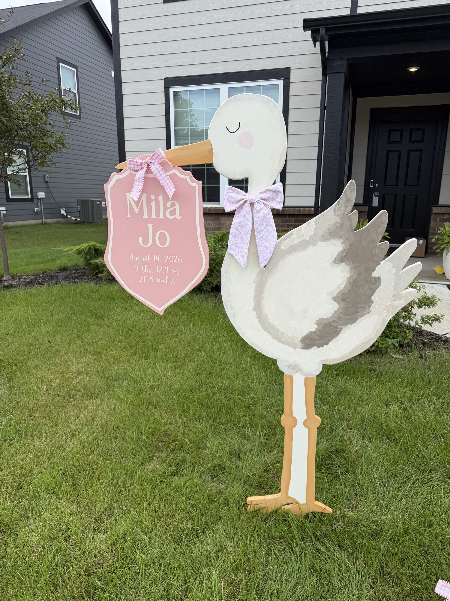 Close view of a hand-painted stork with a pink announcement plaque and floral bow
