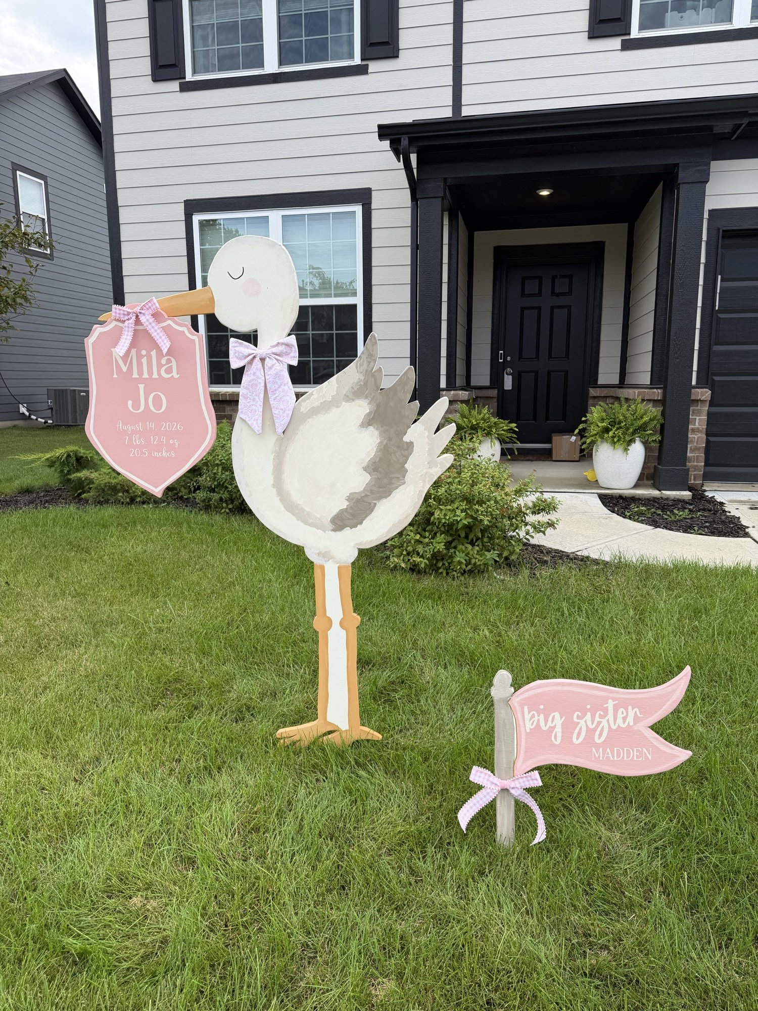 Pink stork announcement and matching big sister flag installed in a front yard