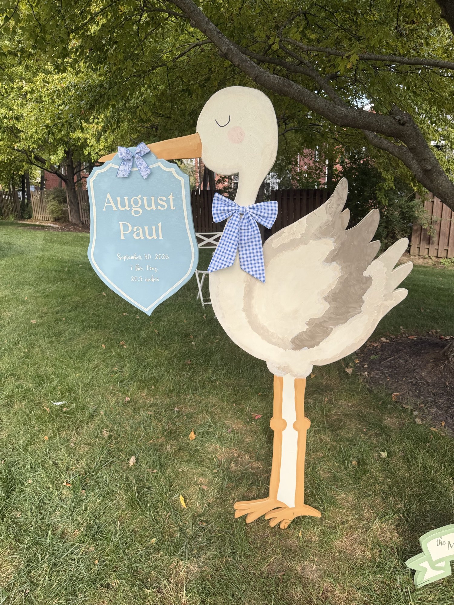 Hand-painted stork with a blue announcement plaque and gingham bow beneath a tree